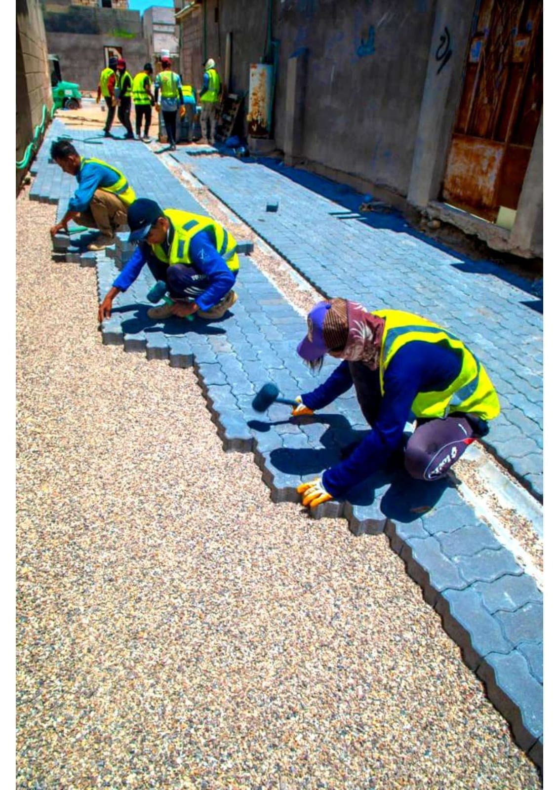 Workers laying interlock paving in a narrow residential lane