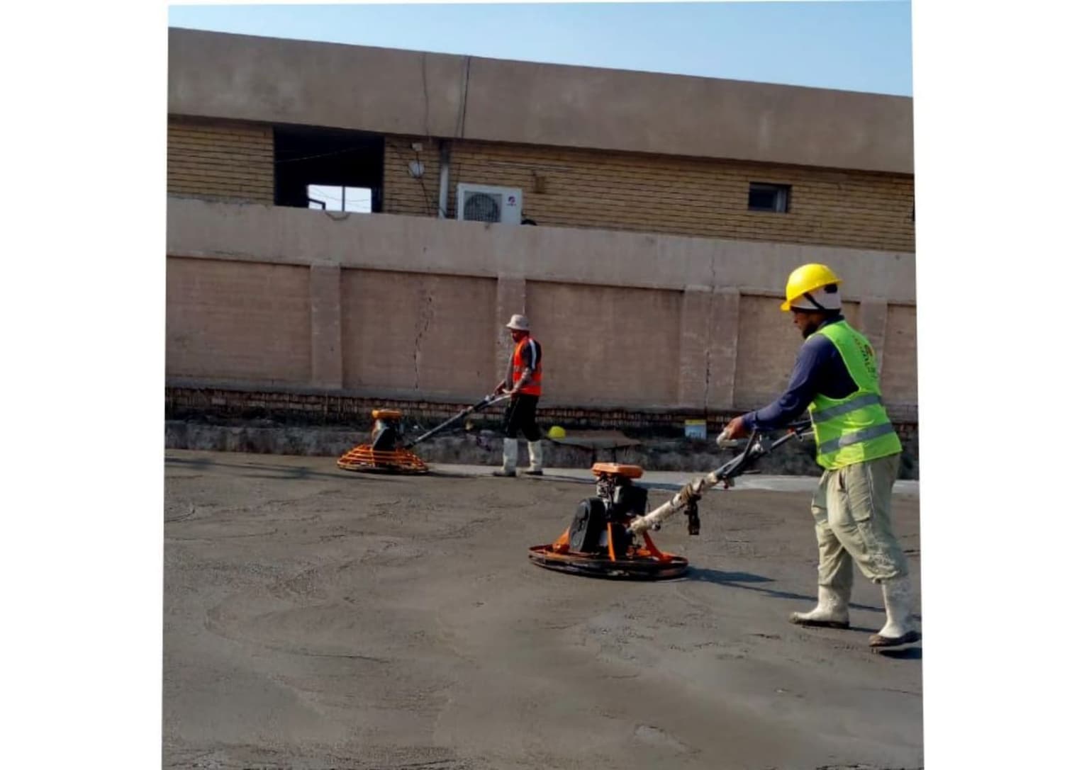 Two workers power-trowelling a fresh concrete floor slab