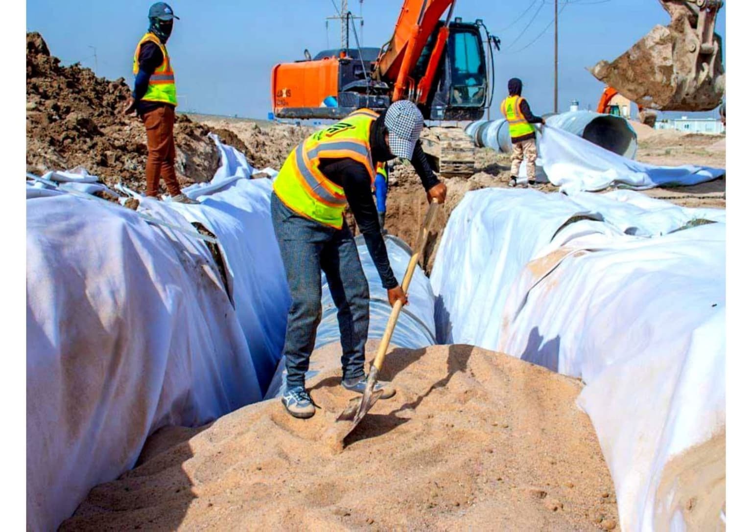 عامل يهيل الرمل فوق أنابيب ملفوفة بالجيوتكستايل داخل الخندق